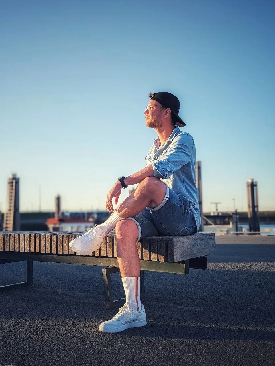 Mann mit Cap sitzt im warmen Abendlicht auf einer Bank am Wasser