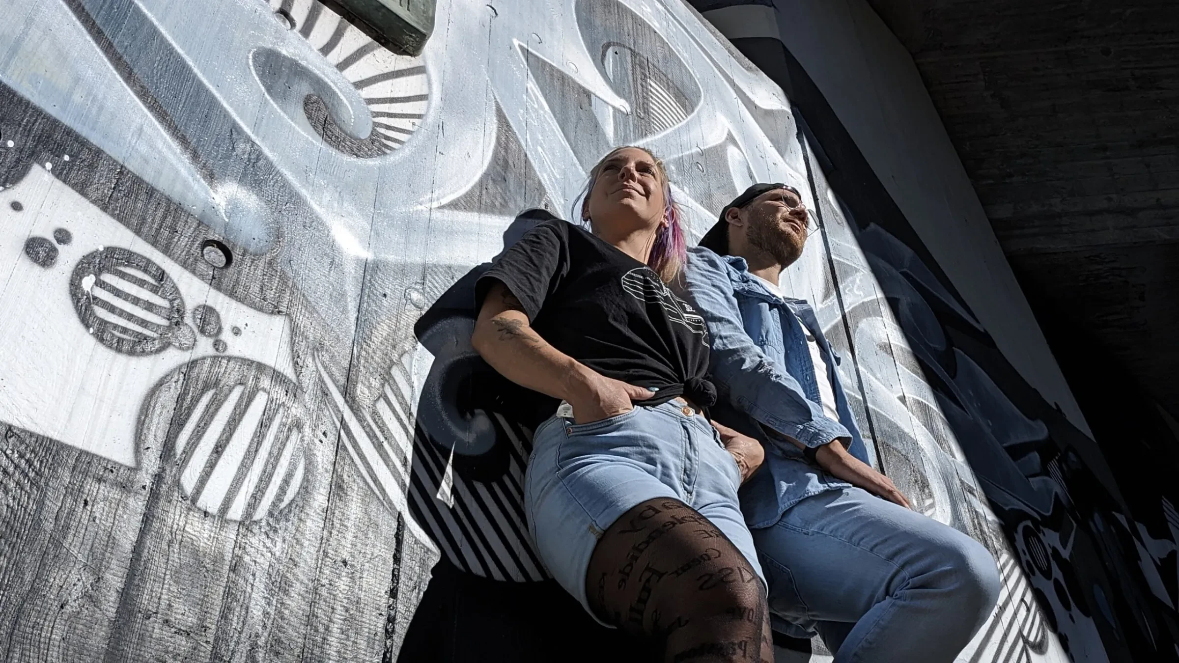 Martin und Larissa lehnen nebeneinander an einer bemalten Betonwand
